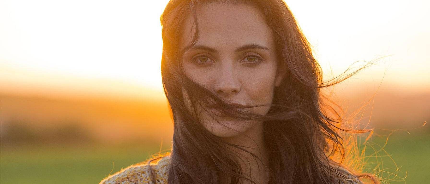 Une femme au coucher du soleil regarde dans la caméra.