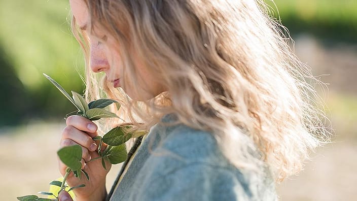 Une femme blonde sent les feuilles d'une plante
