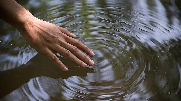 Une main touche doucement une flaque d'eau.