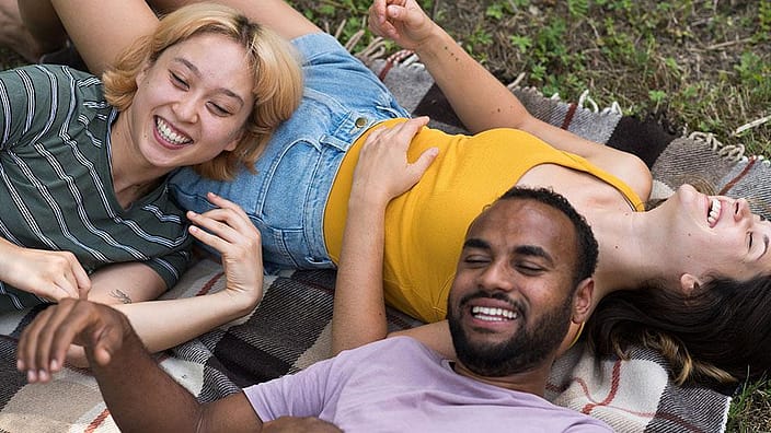 Deux femmes et un homme sont allongés ensemble dans l'herbe.